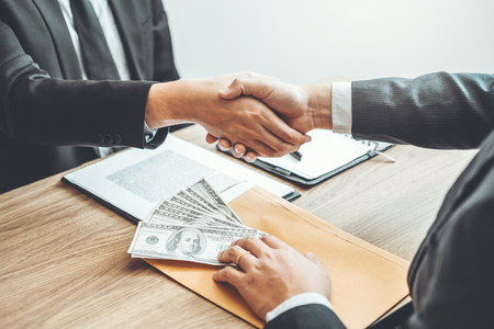 Corruption concept,Business man passing money dollar bills corruption bribery to businessman manager and handshake between two colleagues.の写真素材