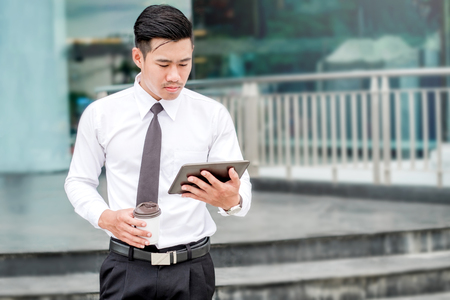 Businessman With Coffee Using Digital Tablet at city outside officeの写真素材