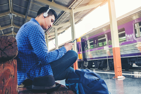 Travel man using mobile listening music phone and at train stationの写真素材