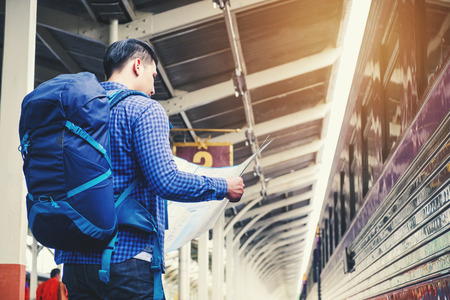 Tourist man backpacker using map to travel at train stationの写真素材