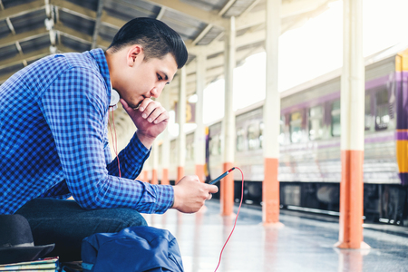 Travel man using mobile listening music phone and at train stationの写真素材