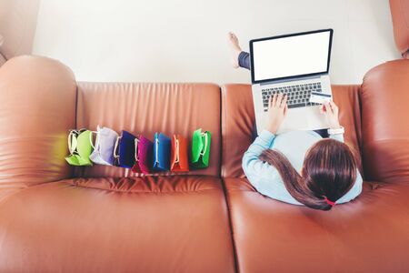 Woman with laptop shopping online with debit card on sofa in homeの写真素材