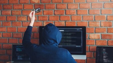 Dangerous Hooded Hacker using credit card typing bad data into computer online system and spreading to global stolen personal information. Cyber security conceptの写真素材