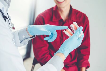 Dentist talking to smiling male patient and showing denture in dental officeの写真素材
