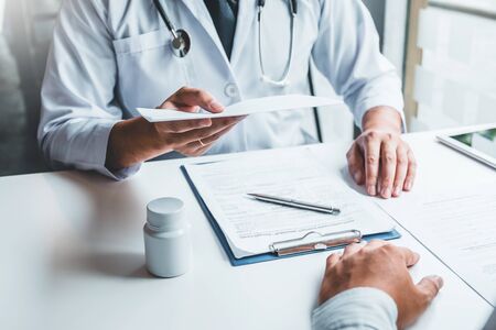 Doctor or physician writing diagnosis and giving a medical prescription to female Patientの写真素材