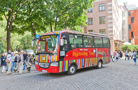 RIGA, LATVIA - JULY 05, 2016: Red city sightseeing bus waiting for tourists near Church of St Peter in Riga, Latvia. Povides excursion tours around old Riga (UNESCO site)のeditorial素材