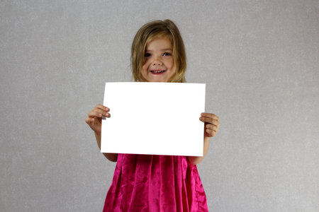 A little girl in a dress holds a white sheet of paper in front of her.の写真素材