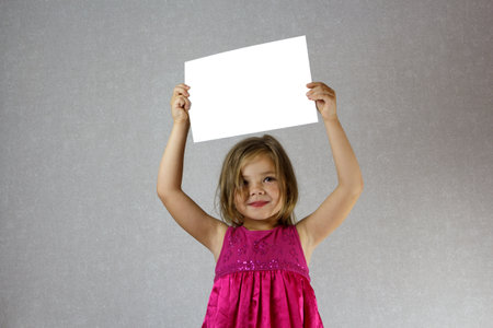 A girl in a pink dress holding a white sheet of paper. Mock up.の写真素材