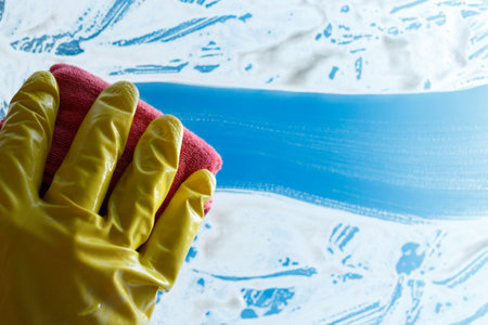 Hand in yellow rubber glove washes soapy glass.の写真素材