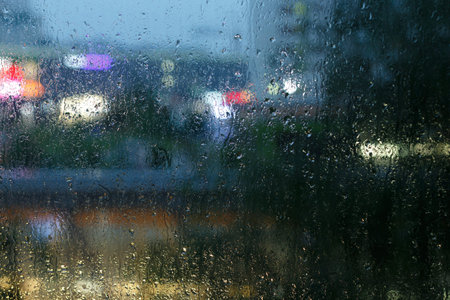 Blurred image of the evening city through the glass with raindrops.