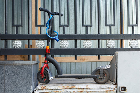 Small black scooter fastened with a blue cable to a steel fence.の写真素材
