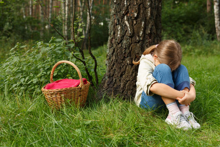 Little girl got lost in the forest with a basket. Sits under a tree.の写真素材