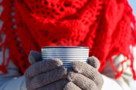 Woman in a red plaid holds a hot drink in a striped ceramic mug. Soft focus, close up.の写真素材