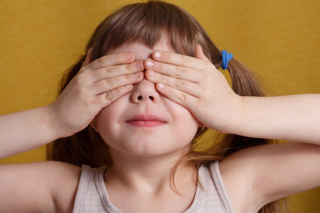 Portrait of a European little girl covering her eyes with her hands. Concept for a surprise, hide and seek game.の写真素材
