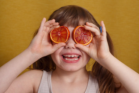 Portrait of a white girl covering her eyes with slices of Sicilian orange. Lifestyle, fun game.の写真素材