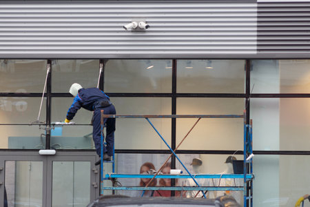 An employee of a cleaning company in blue overalls on a scaffold washes the glass facade of a store.の写真素材