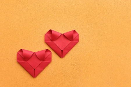 it is couple folding red paper hearts on yellow concrete wall for valentine pattern and background.の写真素材