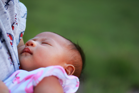 mother holds sleeping newborn baby on arm and breast ourdoor.の写真素材