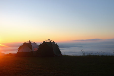 two tents for camping on top of mountain with sea of mist and sunshine in the morning.の写真素材