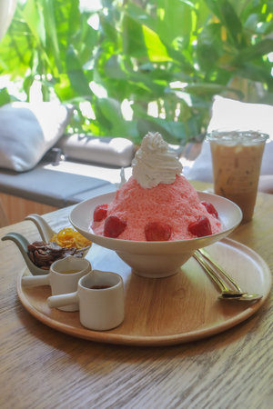 Fruity shaved ice of red strawberry or bingsu on white bowl with toppings,sauce and jam served with iced coffee.の写真素材