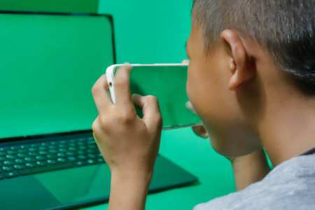 boy with a mobile phone in the hands of a laptop on a green backgroundの写真素材