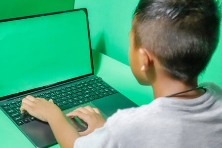 Child using a laptop computer on a green background. Back view.の写真素材