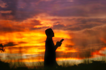Silhouette of a man using a smartphone at sunset in the evening.の写真素材