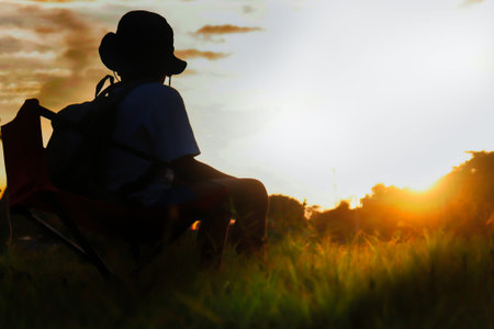 Silhouette of woman sitting on the grass and watching the sunsetの写真素材