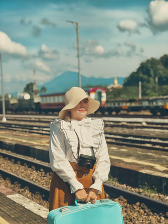 Young woman traveler with suitcase waiting train at railway station. Travel and vacation concept.の写真素材