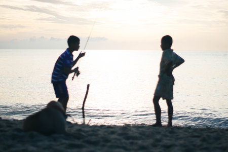 Silhouette of two boys fishing on the beach in the eveningの写真素材