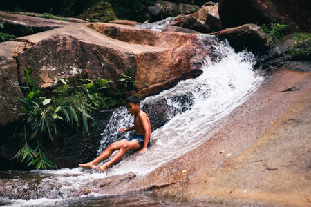 Young boy sitting on the edge of a waterfall in a tropical forestの写真素材