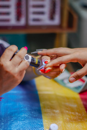 Manicurist applying red nail polish on female fingernails