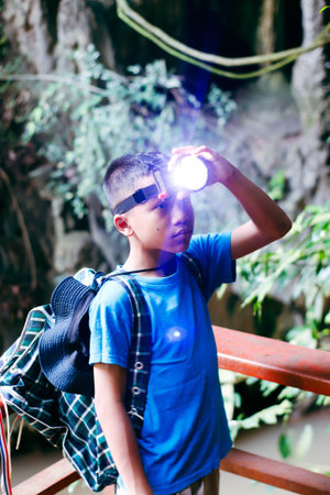 A boy is standing on a wooden bridge, holding a flashlight, and looking to the left.