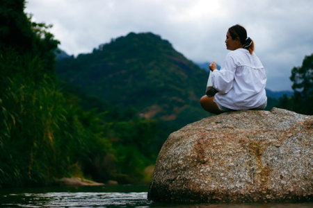 Young woman meditating on a rock in the middle of the river