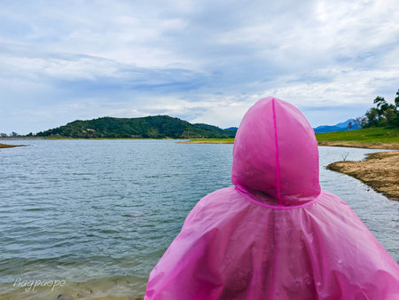 Girl in pink raincoat standing on the shore of the lake.の写真素材