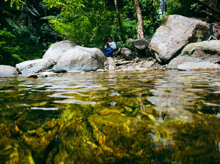 Woman sitting on the rock in the river and looking at the waterの写真素材