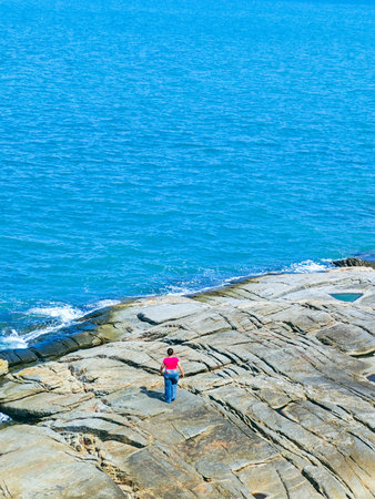 Person standing on the rock and looking at the sea in summerの写真素材