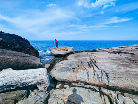 Man standing on the rock and looking at the sea with blue skyの写真素材