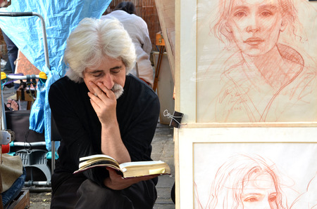 PARIS / FRANCE - September 24, 2011: Artist read a book in Montmartre, the legendary bohemian artist district of Paris. Next to the painter stands his work.のeditorial素材