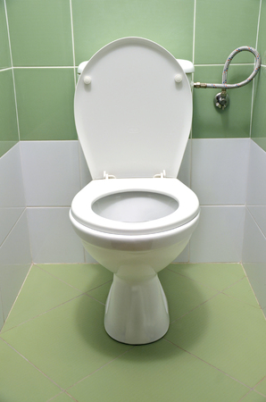 Flush toilet with white and green tiles in background, front viewの写真素材