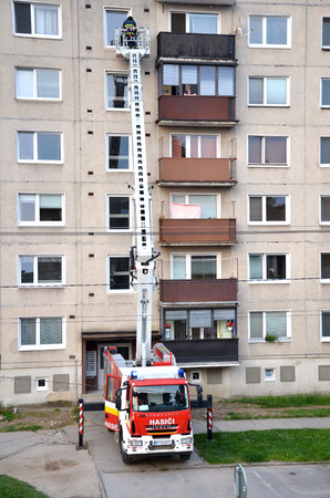 Bytca, Slovakia - June 4, 2016: Firefighters in action, a man uprise in telescopic boom basket of fire truck. Block of flats in background.のeditorial素材
