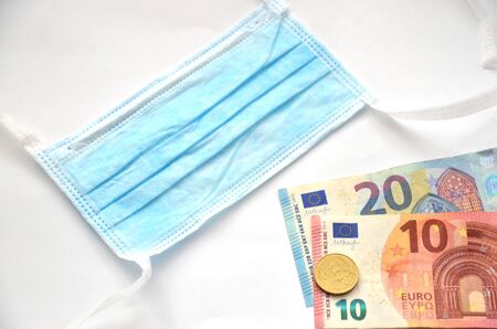 Surgical mask next to euro money on white backgroundの写真素材