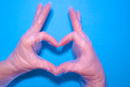 Womens hands in transparent household gloves represent the heart on a blue background. Hand protection.の写真素材