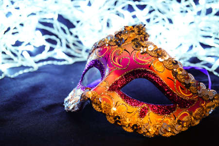 Purple and yellow carnival mask on black silk. There are festive white lights in the background.の写真素材
