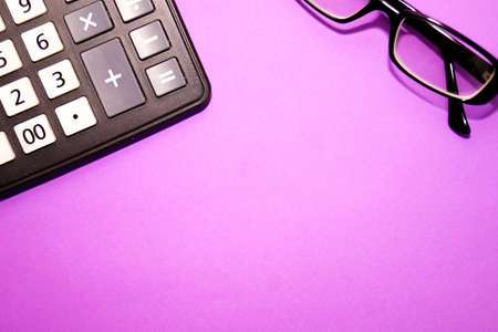 Black glasses and a calculator lie on a purple background. A space for creativity. Top view.の写真素材