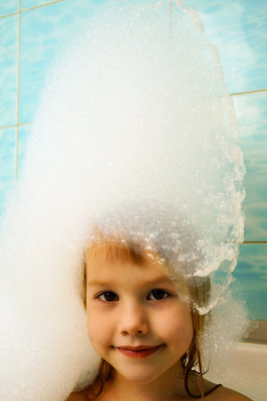 A cute baby in the bath is washing with soap foam. On his head is an improvised foam hat.