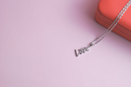 Silver pendant in shape of inscription love on red box. Pink background. Valentines Day, birthday,...