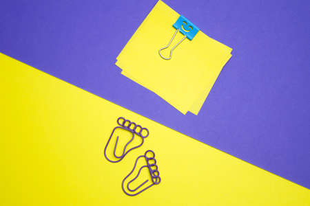 Paper clips in the shape of a foot, located on a yellow background. Yellow sheets on a purple background, secured with a paper clip in the shape of a smile.の写真素材
