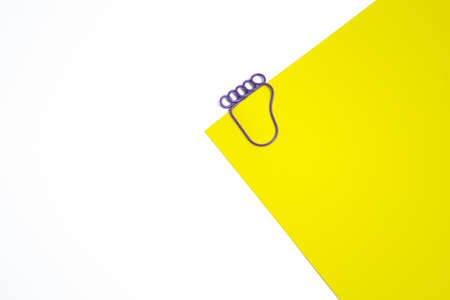 Yellow blank with a paper clip on a white background. A paper clip in the shape of a foot.の写真素材