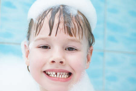 A charming baby is washing in the bathroom, soap foam on her head. A smile on his face. Portrait.の写真素材